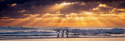 三个人手持冲浪板面对海浪
